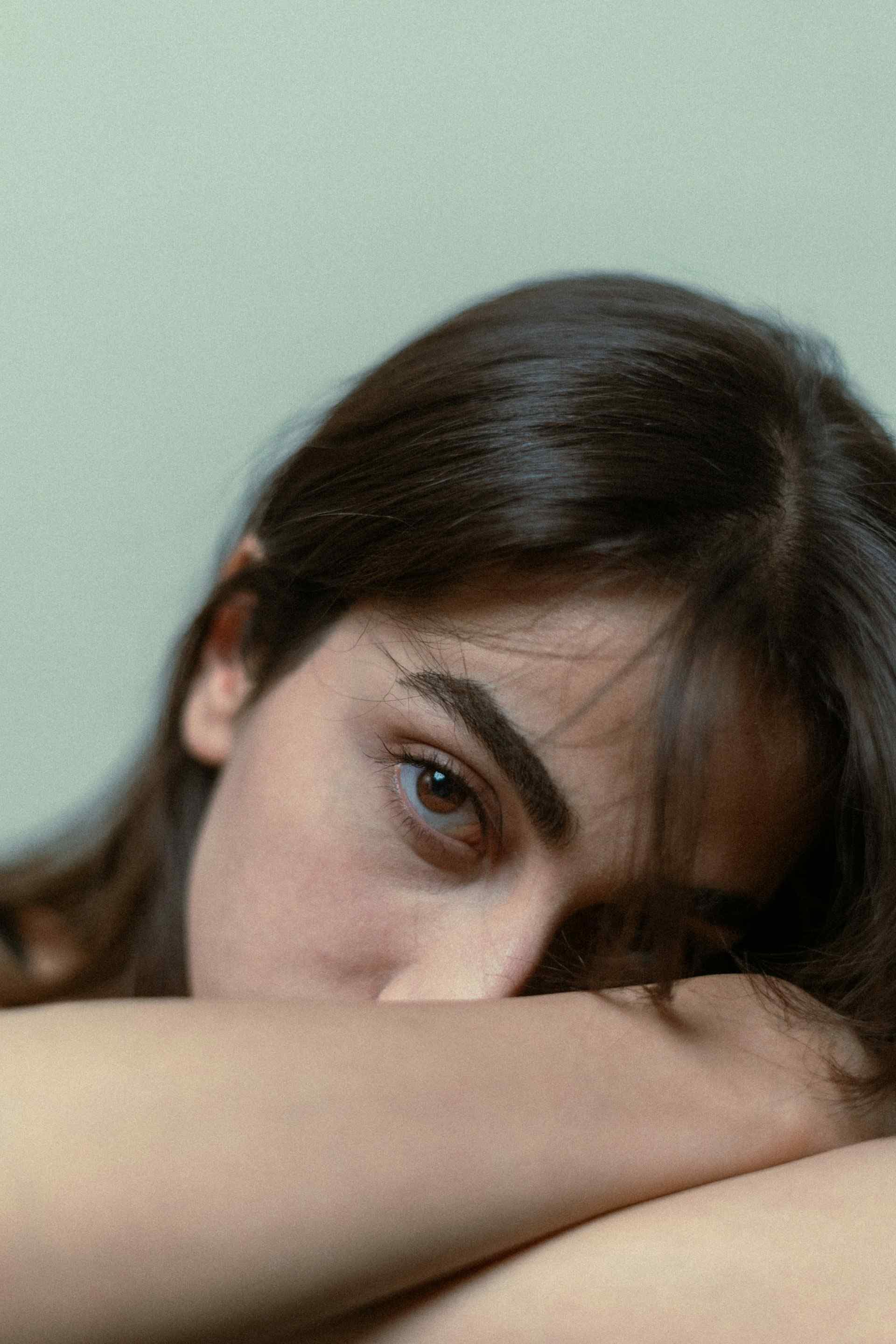 Eine junge Frau schaut in die Kamera, während sie den Kopf auf den Armen legt.