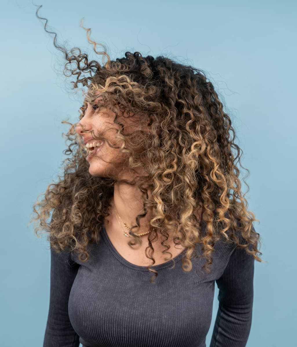 Eine junge Frau vor einem blauen Hintergrund, während die braunen Haare nach oben wehen