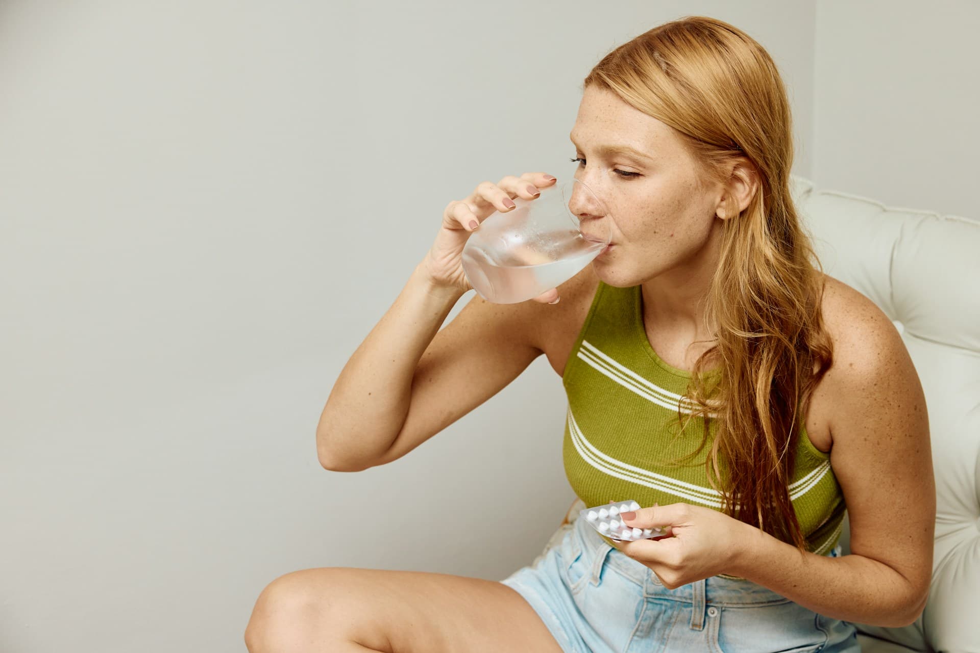 Eine Frau hält Tabletten in der Hand und trinkt ein Glas Wasser.